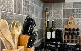 Modern kitchen decor setup with wooden utensil holder, knife block, spice rack, candles, and mini plants on a woven mat. home decor items for kitchen